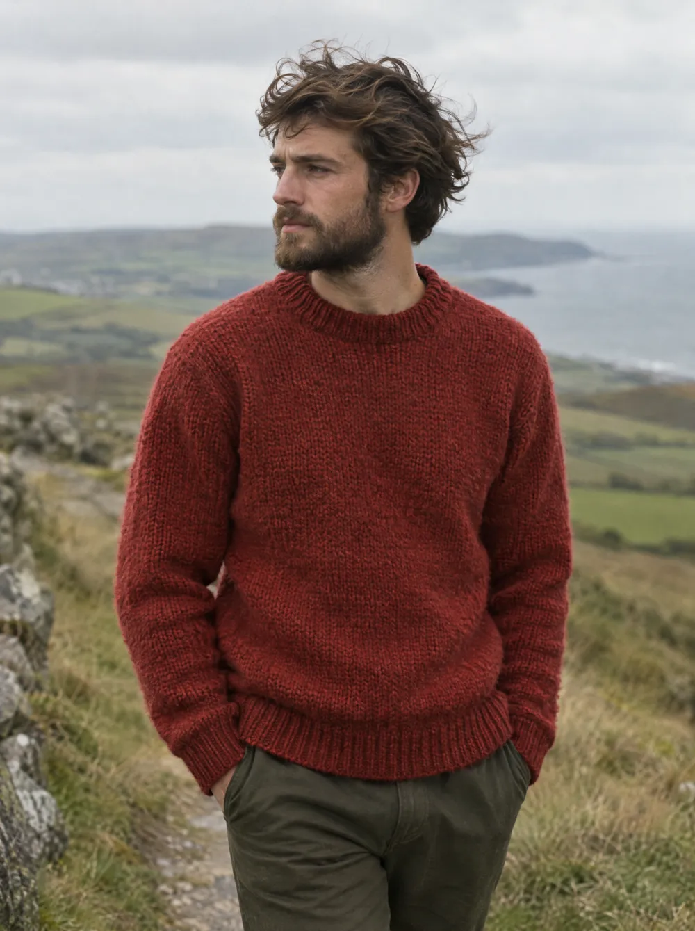 Ein Mann im krapproten Wollpullover auf einem windigen Weg über dem Meer