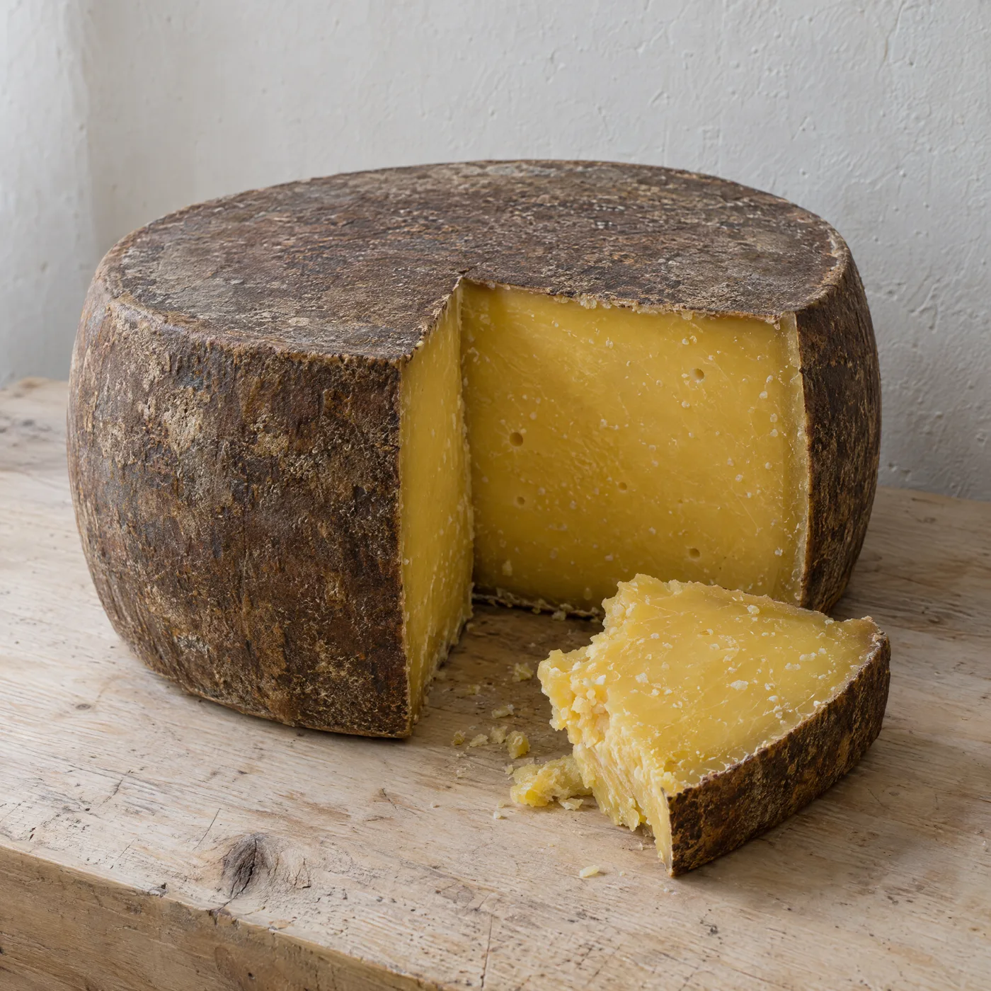 Großer Bergkäse aufgeschnitten, dichter goldgelber Teig, dunkelbraune Rinde, ein abgebrochenes Stück davor
