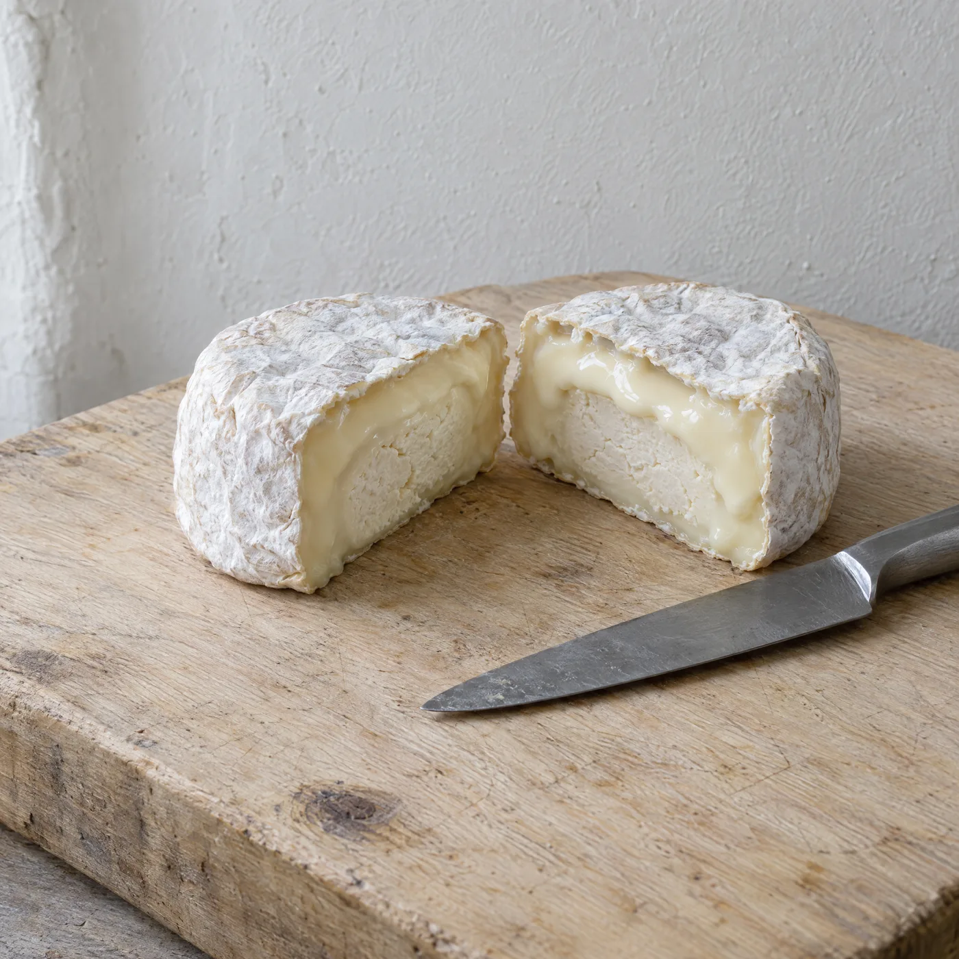 Kleiner Weichkäse mit weißer Rinde, halbiert, innen cremig und unter der Rinde weich laufend