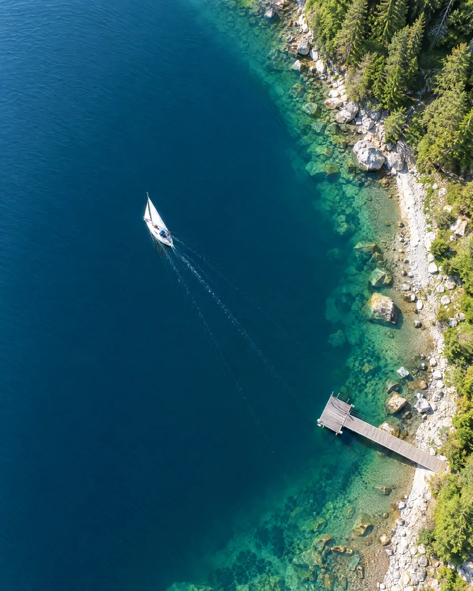 Luftbild von oben: Bergsee mit einem Segelboot und seiner langen Spur